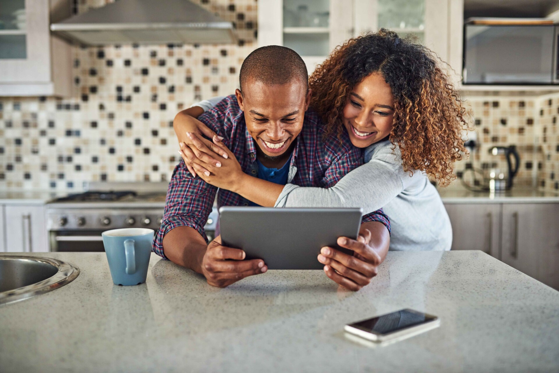 A man and woman in a kitchen are reviewing their online banking details on a tablet together.