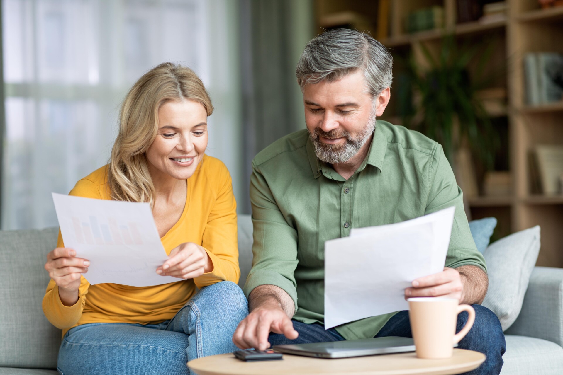 A cheerful couple examines documents while using a calculator, enjoying their time together while discussing important information regarding retirement and IRAs.