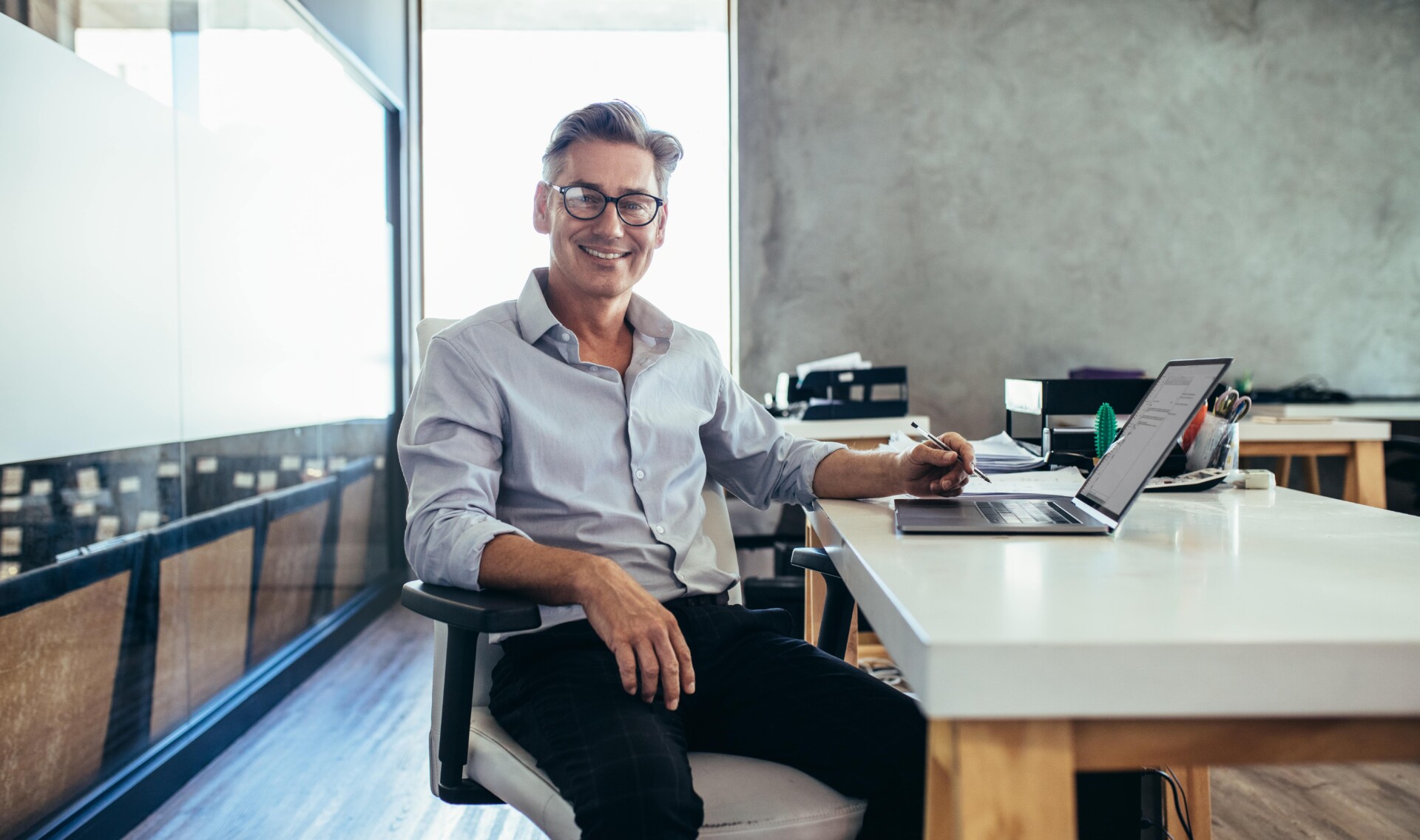 A man wearing glasses sits at a desk, focused on his laptop, with documents about extended deposit insurance nearby.