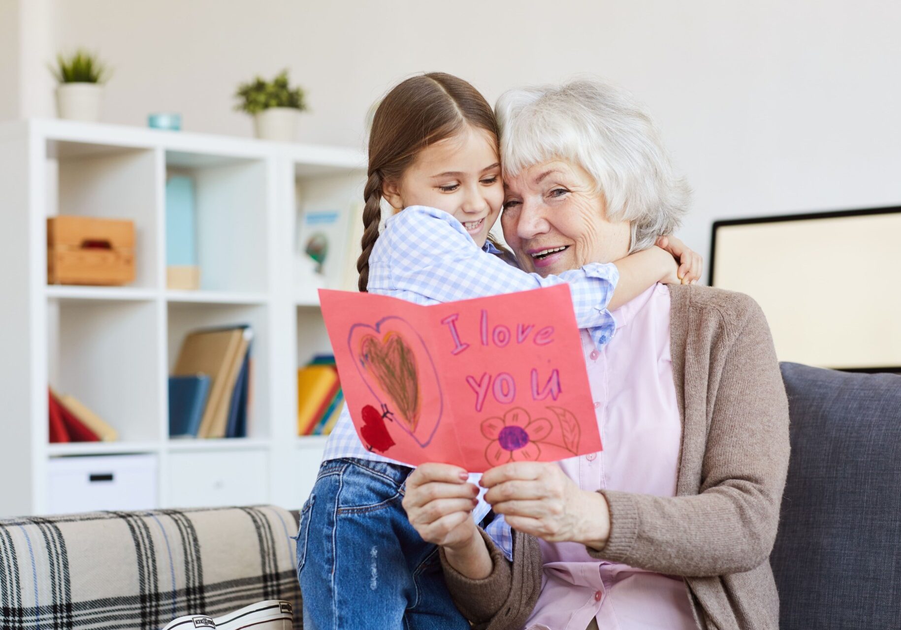 Granddaughter hugs her grandmother while giving a handmade Valentine’s card, a budget-friendly Valentine’s Day idea.