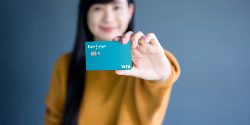 "A young woman holding a Park View Visa credit card, smiling and presenting it towards the camera.